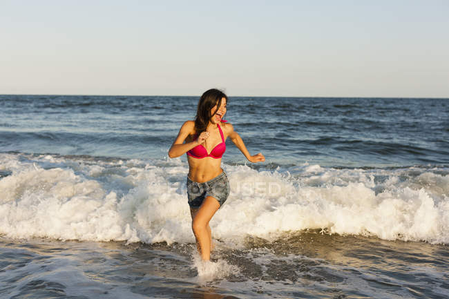 Mujer joven corriendo en el borde del agua en la playa en Atlantic City, EE.UU. . - foto de stock