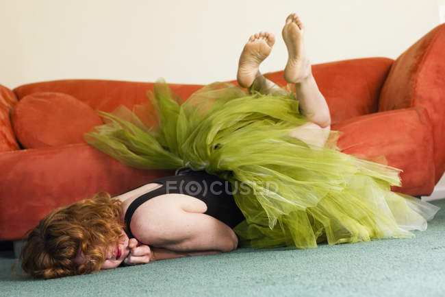 Woman in lime green tutu lying on front on floor and kicking legs in air. — Stock Photo