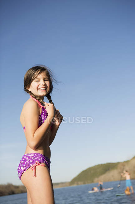 Pre-adolescent girl on jetty with paddleboarders in background. — Stock Photo