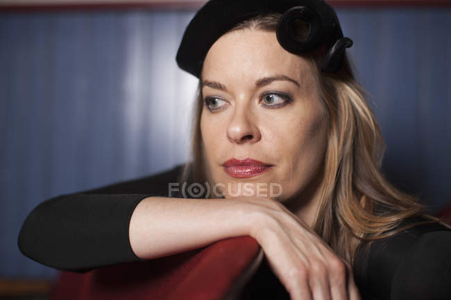Woman in elegant hat resting chin on hand and looking away in theater. — Stock Photo