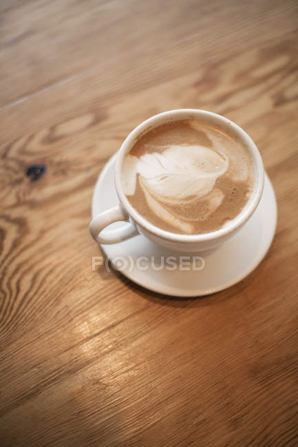 Xícara de cappuccino espumoso na xícara com pires na mesa de madeira . — Fotografia de Stock
