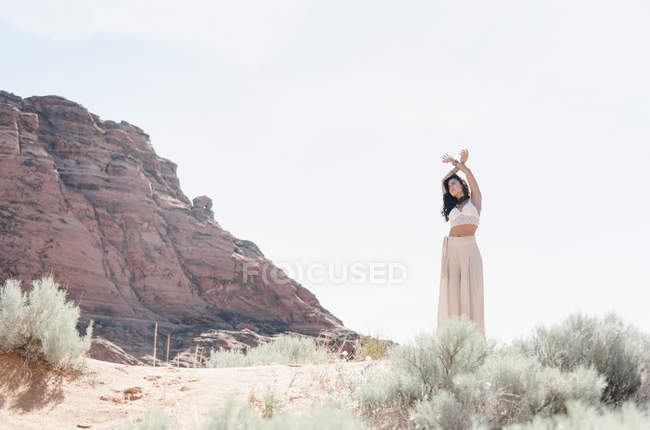 Jovem mulher vestindo vestido branco longo em pé na pradaria com os braços levantados . — Fotografia de Stock