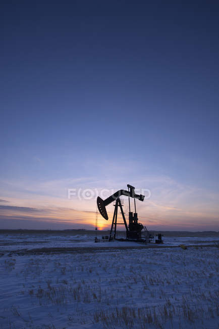 Oil drilling rig and pumpjack on flat plain in Canadian oil field at sunset. — Stock Photo