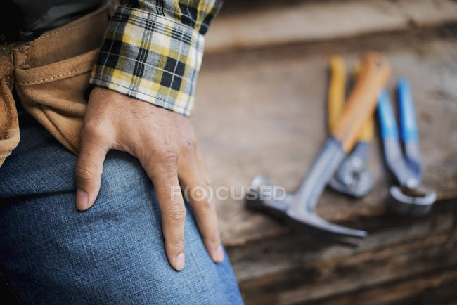 Cropped view of man sitting at workbench with grippers and pliers lined up on plank of wood. — Stock Photo