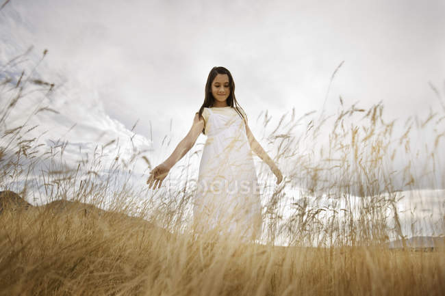 Елементарний вік дівчини в білому платті, що стоїть в траві з розтягнутими руками — стокове фото