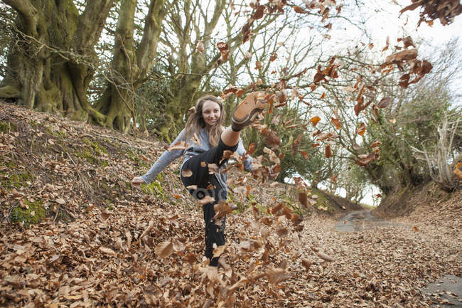 Junge Frau tritt in Herbstwald gegen umgestürzte Blätter. — Stockfoto
