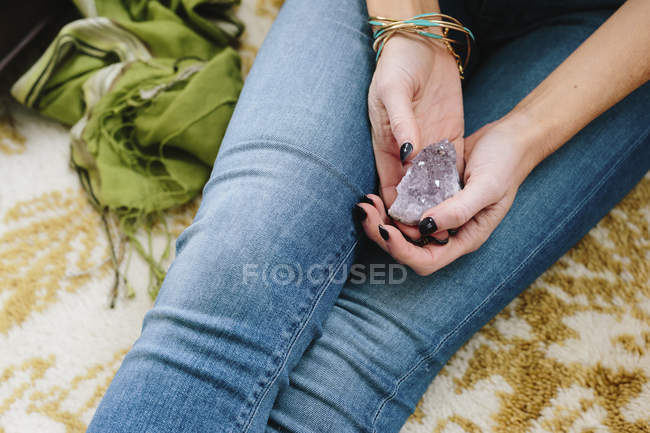 Cropped view of woman sitting and holding small purple crystal in hands. — Stock Photo