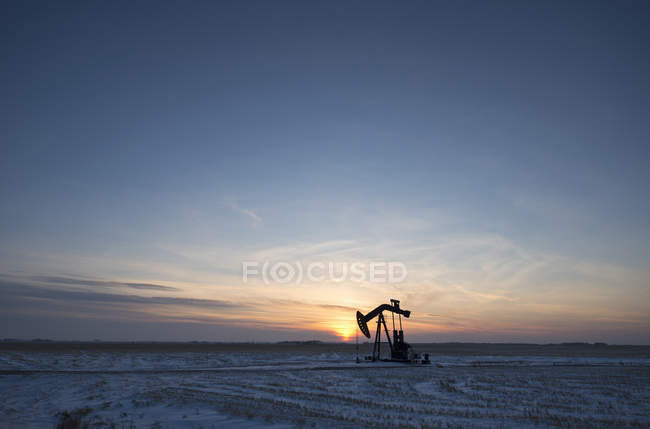 Impianto di perforazione petrolifera e pompetta sulla pianura piatta nel giacimento petrolifero canadese al tramonto . — Foto stock