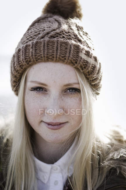 Portrait of teenage girl with freckles in bobble hat on beach. — Stock Photo