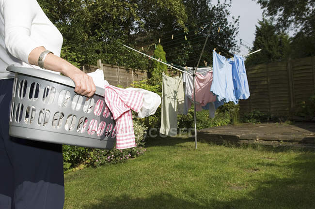Cropped view of woman carrying basket of laundry to washing line. — Stock Photo