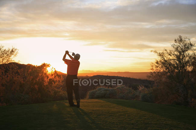 Гравець у гольф teeing off в захід сонця на поле для гольфу. — стокове фото