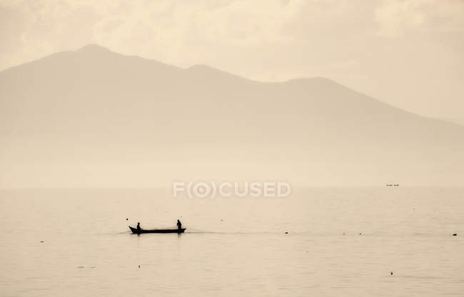 Small fishing boat with two people on Lake Chapala with mountains in background, Mexico. — Stock Photo
