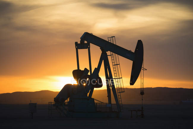Pumpjack working at oil drilling site at sunset. — Stock Photo