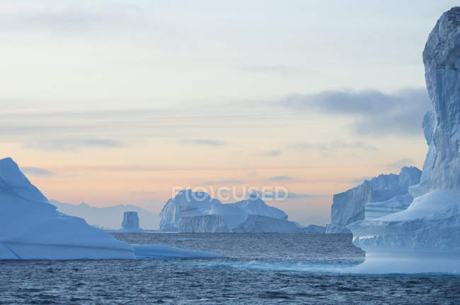 Sonnenuntergangshimmel und schwebende erodierte Eisberge am Sundfjord. — Stockfoto