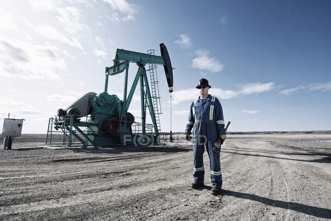 Чоловік в комбінезоні і жорсткий капелюх на гнізді насоса у відкритому грунті на місці видобутку нафти . — стокове фото