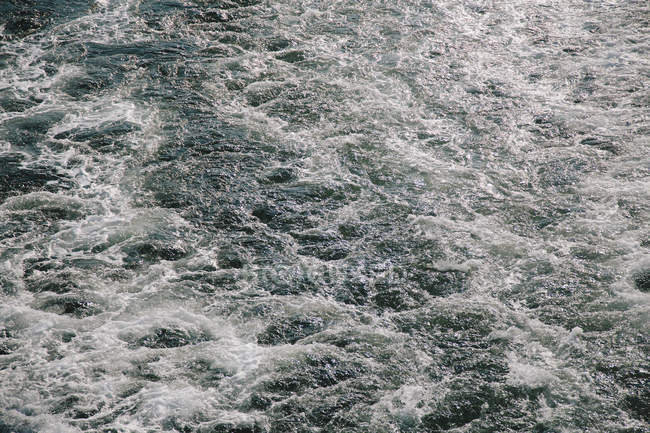 Turbulente Wasseroberfläche mit Wellen und Blasen, Vollbild. — Stockfoto