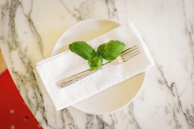 Marble tabletop and napkin with basil leaves and fork. — Stock Photo