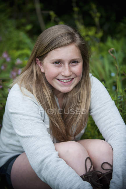 Chica adolescente sentada en el prado del jardín y abrazando las rodillas . - foto de stock