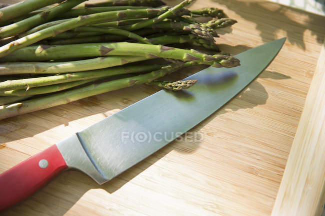 Manojo de espárragos orgánicos recién recogidos en la tabla de cortar con cuchillo de cocina afilado . - foto de stock