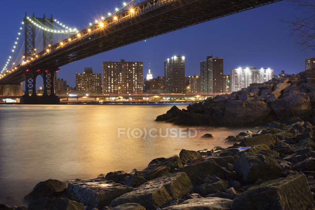 Vista noturna em direção a Manhattan com a Ponte Manhattan abrangendo East River, Nova York, EUA . — Fotografia de Stock