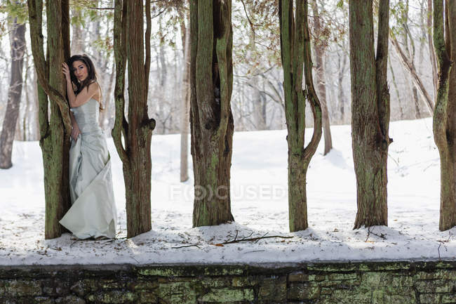 Jovem mulher em vestido de baile ao ar livre na neve entre árvores . — Fotografia de Stock