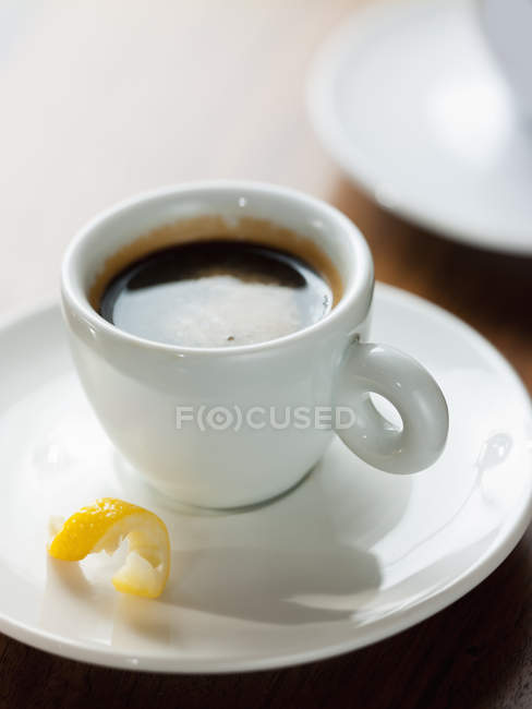 Nahaufnahme einer Tasse schwarzen Kaffees in weißer Tasse mit Zitronenschale in Untertasse. — Stockfoto