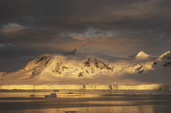 Sonnenuntergang über der bergigen Landschaft der Antarktis und der Wasseroberfläche. — Stockfoto