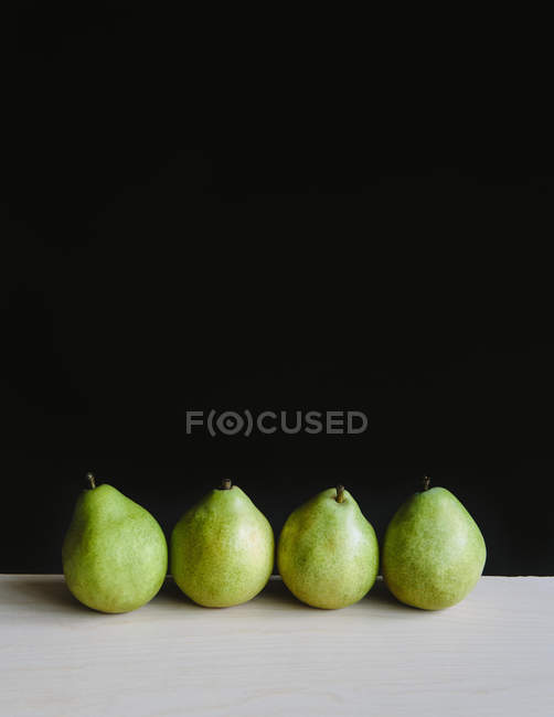 Row of four green Anjou pears on table — Stock Photo