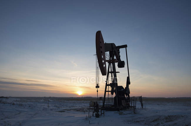 Oil drilling rig and pumpjack on flat plain in Canadian oil field at sunset. — Stock Photo