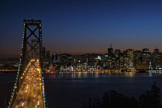 Bridge at night with traffic lit up and lights of settlements along shore of bay in San Francisco, USA. — Stock Photo