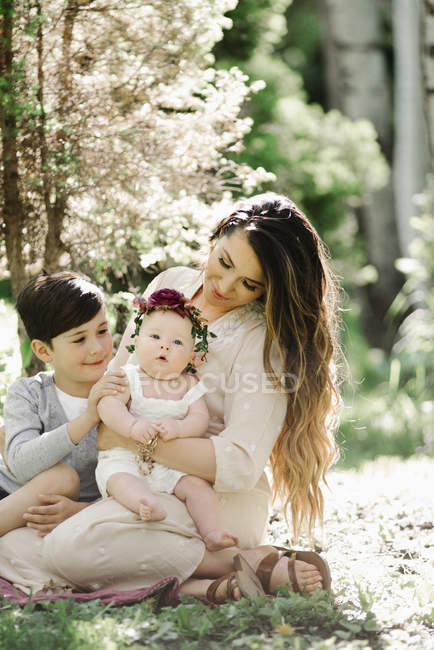 Mère souriante assise dans le jardin avec garçon et bébé fille avec couronne
. — Photo de stock