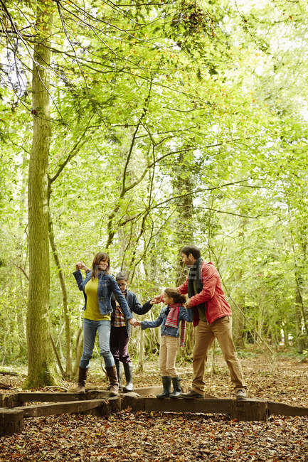 Family in warm coats balancing on wooden log in beech woods in autumn. — Stock Photo
