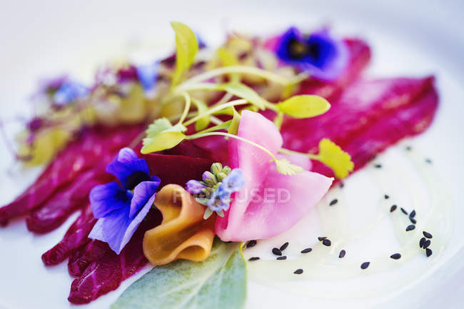 Carpaccio y guarnición de brotes de guisantes frescos y flores comestibles en plato blanco . - foto de stock