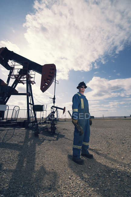Hombre en overol y sombrero duro en gato de la bomba en campo abierto en el sitio de extracción de aceite . - foto de stock
