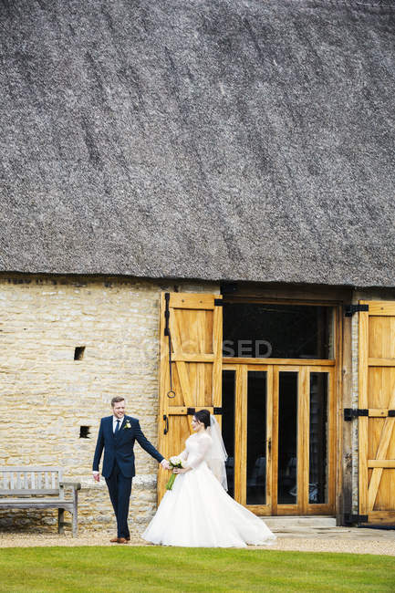 Bride and groom walking hand in hand from barn. — Stock Photo