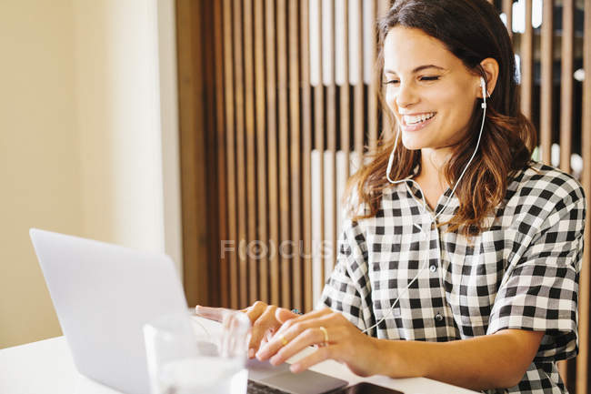 Mujer en auriculares trabajando en el ordenador portátil y riendo en el interior . - foto de stock