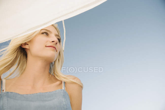 Portrait of blonde young woman under sail on boat against blue sky. — Stock Photo