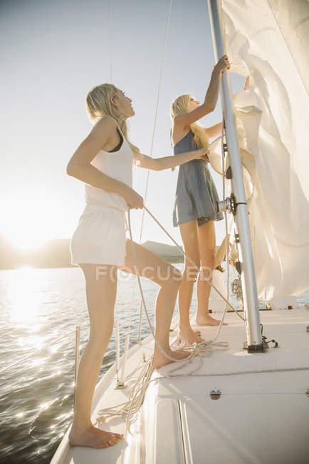 Two teenage sisters adjusting sail on sailboat at lake. — Stock Photo
