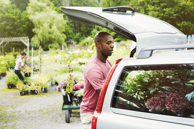 Mann lädt Blumen in Kofferraum eines vor Gartencenter geparkten Autos. — Stockfoto