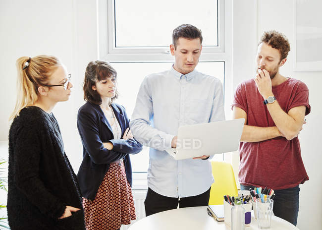 Coworkers standing around table at business meeting and looking at laptop. — Stock Photo