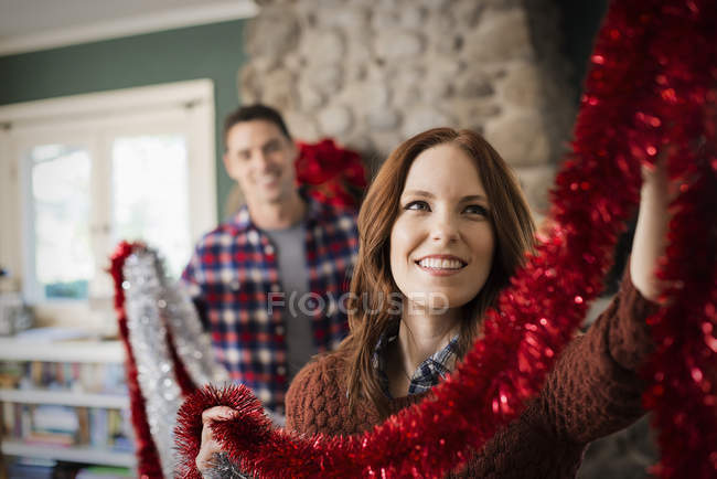 Pareja joven colgando oropel y decorando la casa en Navidad . - foto de stock