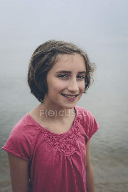 Portrait of smiling pre-adolescent girl in front of lake water. — Stock Photo