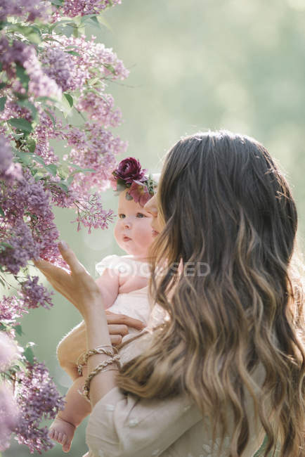 Mother holding baby girl with flower wreath in garden. — Stock Photo