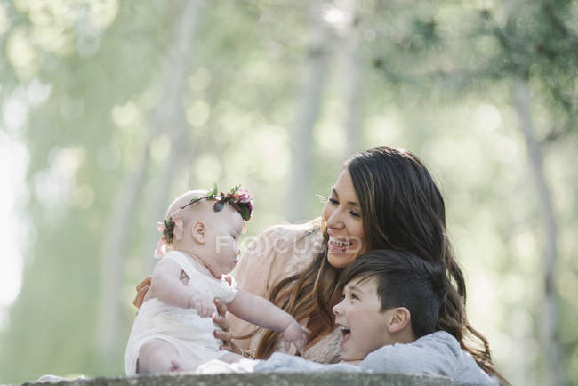Sonriente madre con hijo e hija bebé con corona de flores al aire libre . - foto de stock