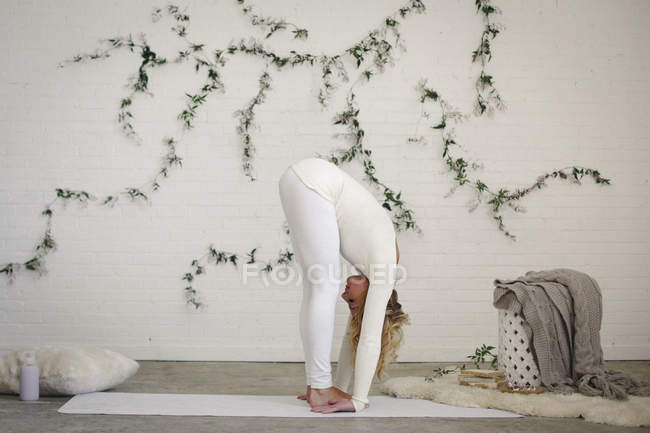 Блондинка наклоняется вперед на белом коврике для йоги . — стоковое фото