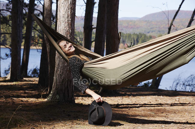 Mulher relaxante em rede sob pinheiros por lago . — Fotografia de Stock