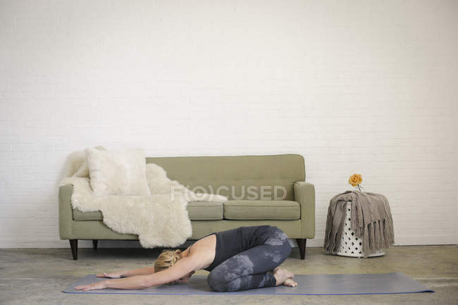 Blonde woman kneeling on yoga mat in child pose. — Stock Photo