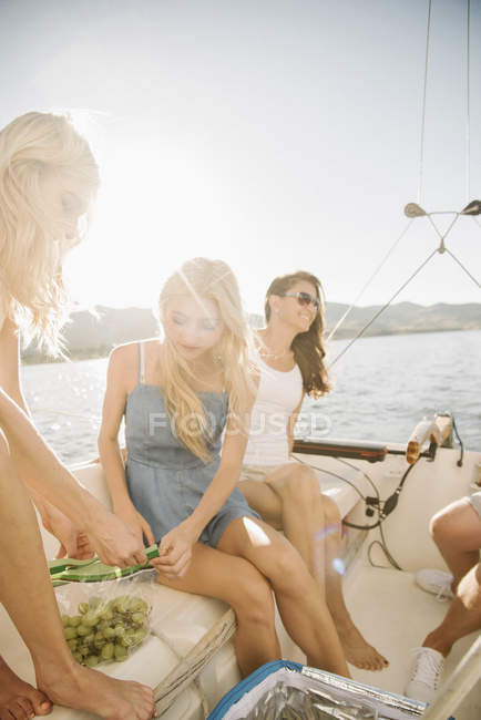 Madre con figlie adolescenti che mangiano uva sulla barca a vela . — Foto stock