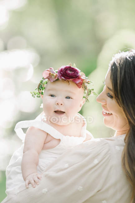 Mid adult woman posing with baby daughter with flower wreath outdoors. — Stock Photo