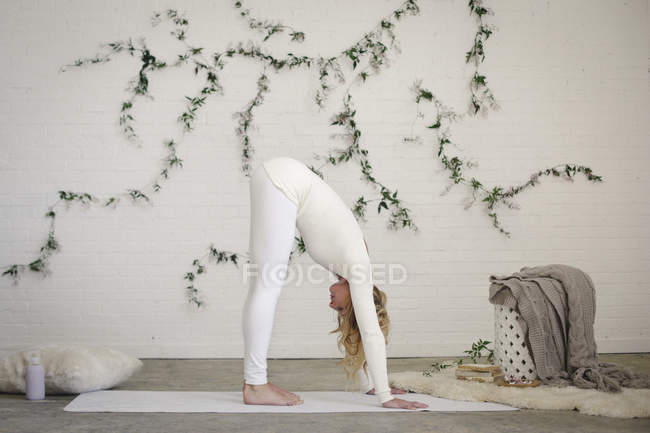 Blonde woman bending forward on white yoga mat. — Stock Photo